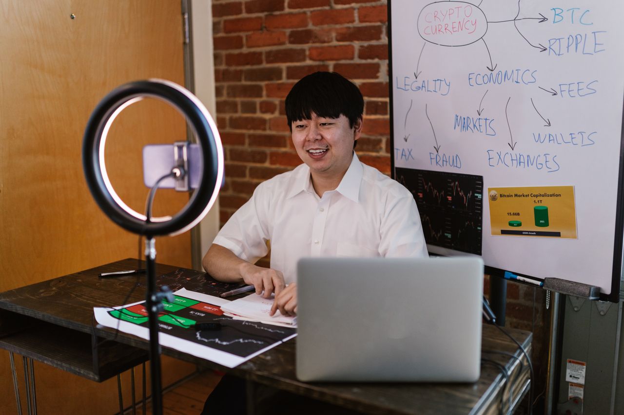 services-04 Man discussing cryptocurrency economics with ring light and laptop, engaging content creation.