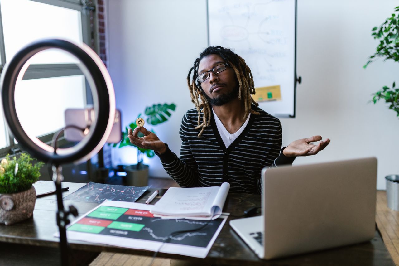 heros-img A man in a home office setting holds a bitcoin, discussing cryptocurrency trading.